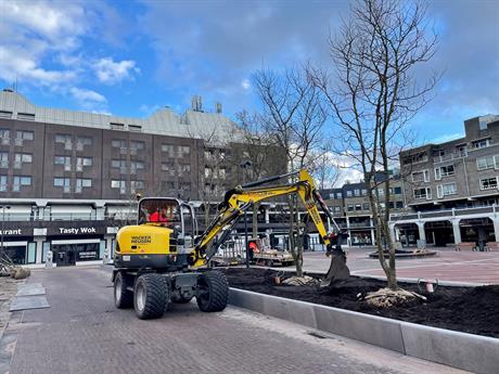 Een graafmachine helpt bij het planten van bomen op het vernieuwde Agorahof in het Stadshart van Lelystad