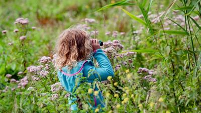 Meisje met verrekijker in veld met bloemen
