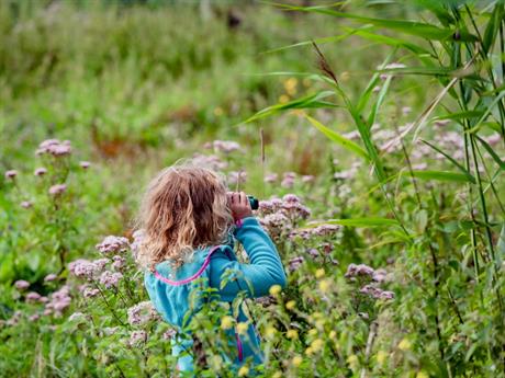 Meisje met verrekijker in veld met bloemen